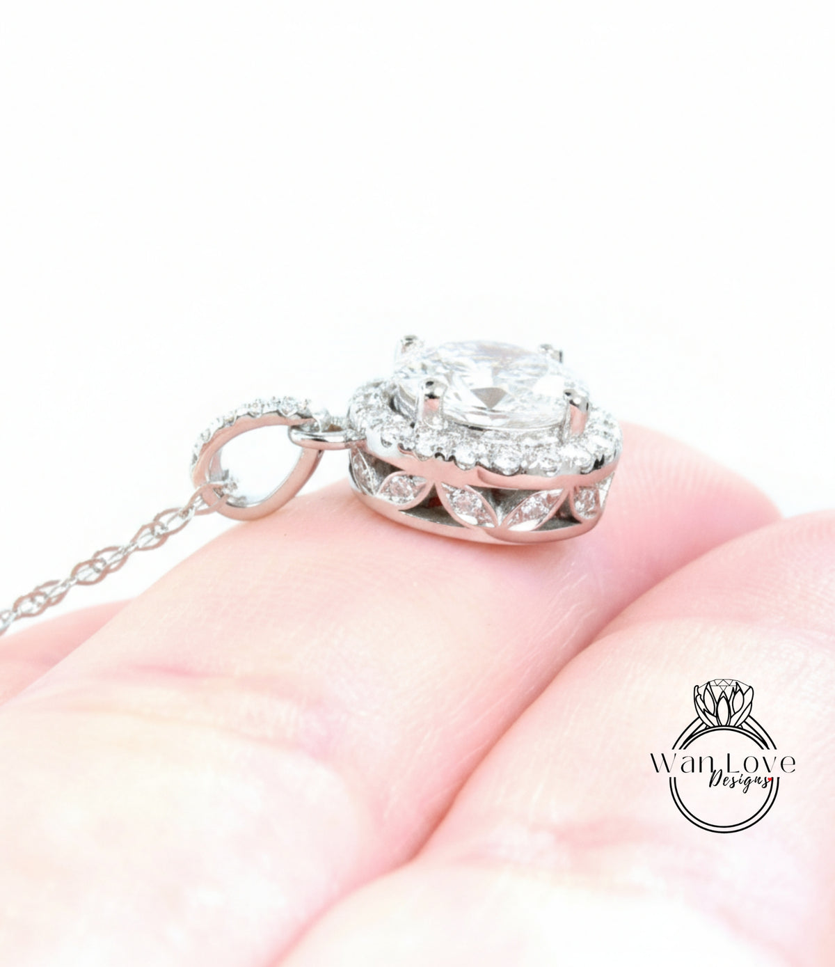 A close-up image of a person's hand holding a delicate silver necklace with a large, sparkling diamond pendant.