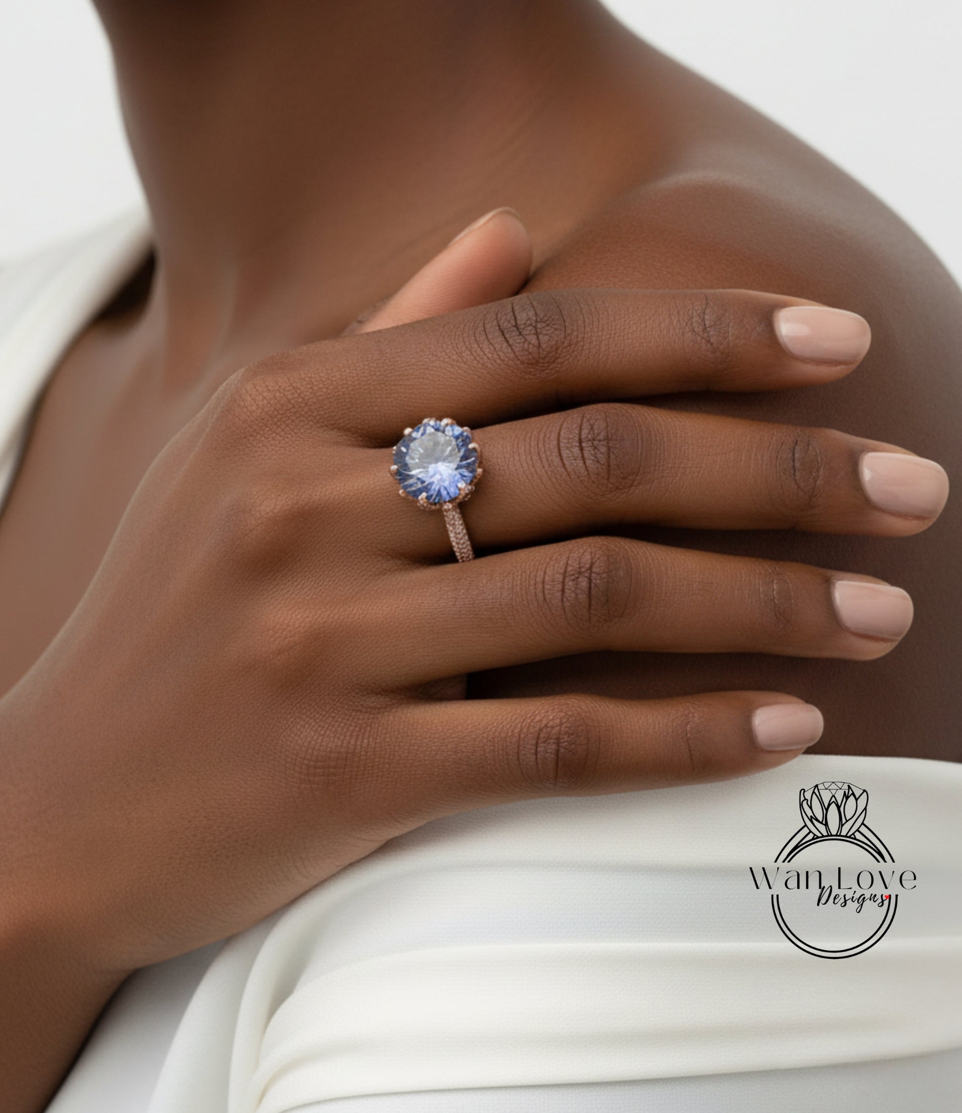 A close-up of a person's hand wearing a ring with a large blue gemstone, resting on a white fabric.