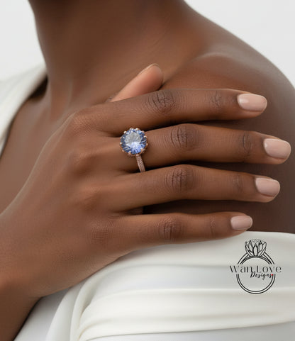 A close-up of a person's hand wearing a ring with a large blue gemstone, resting on a white fabric.