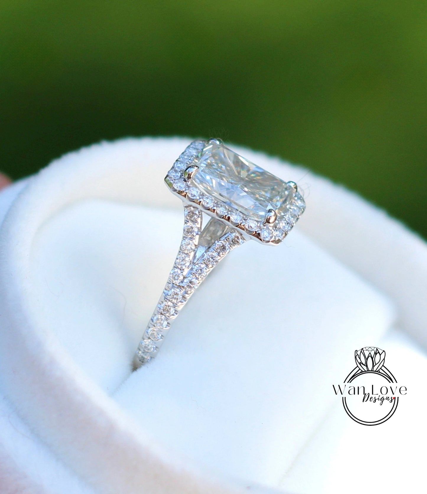 A close-up image of a diamond engagement ring with a large central diamond surrounded by smaller diamonds on the band, placed on a white fabric background.