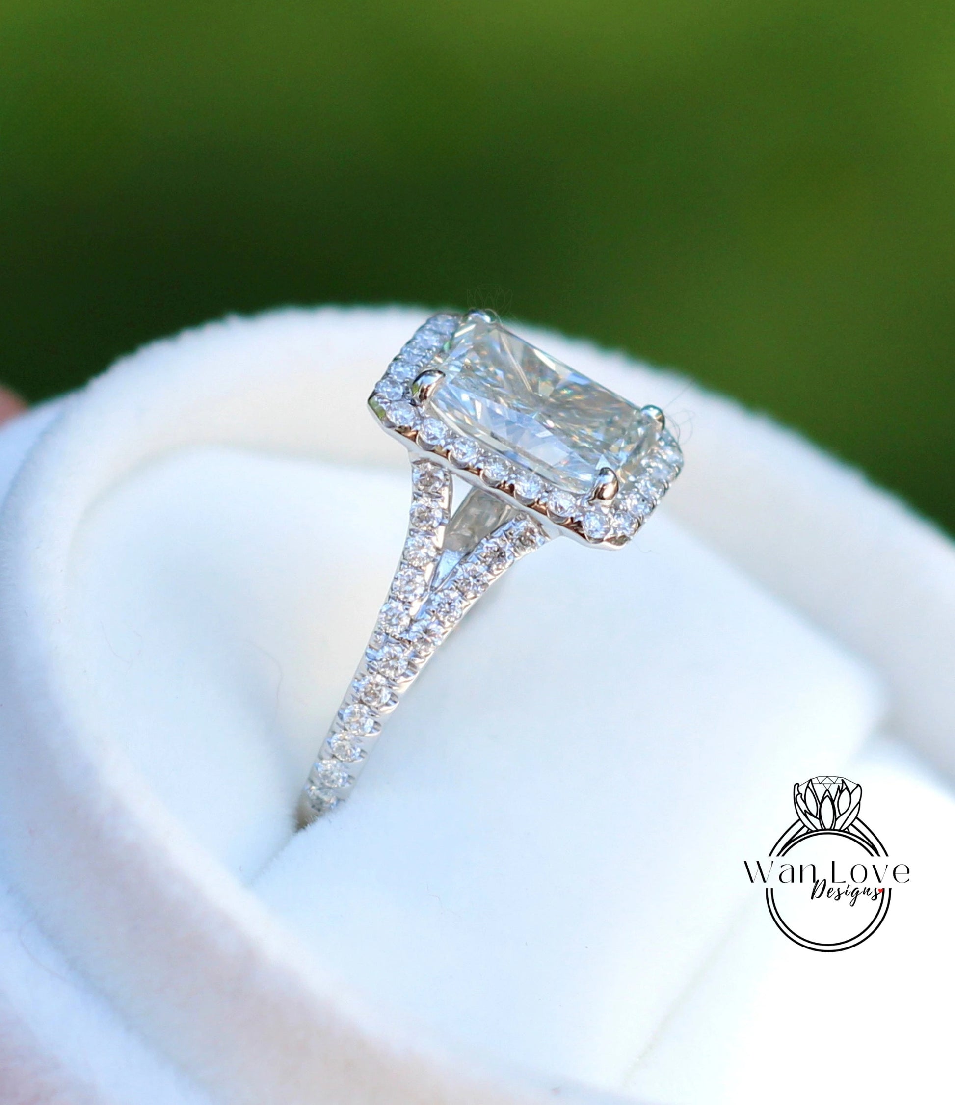 A close-up image of a diamond engagement ring with a large central diamond surrounded by smaller diamonds on the band, placed on a white fabric background.