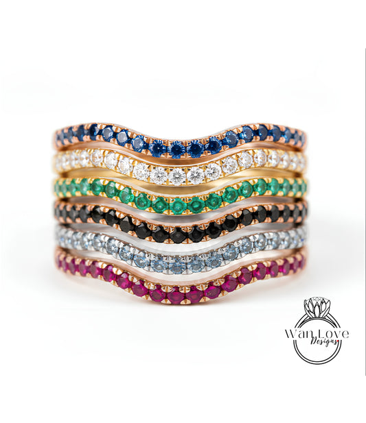 A stack of rings with various colored gemstones, including blue, green, red, and white stones, arranged in a wavy pattern.