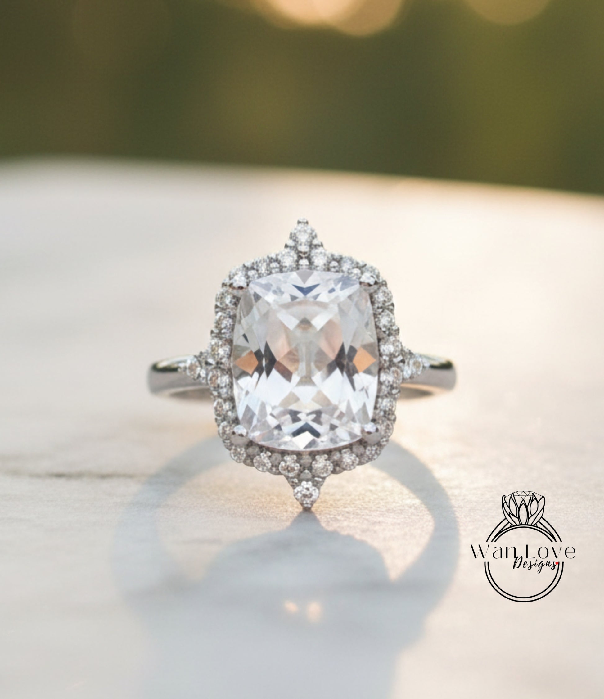 A large, clear gemstone ring with a halo of smaller diamonds around the center stone, set in a silver band, is displayed on a white surface.
