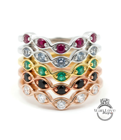 A stack of rings with various colored gemstones, including red, green, and white stones, set in a rose gold band.