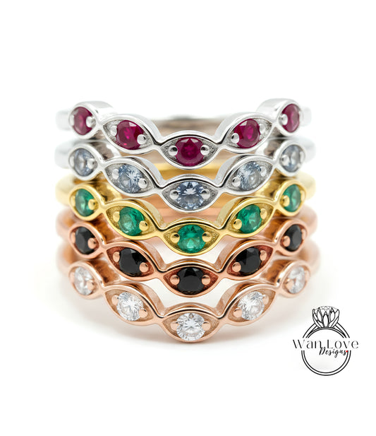 A stack of rings with various colored gemstones, including red, green, and white stones, set in a rose gold band.