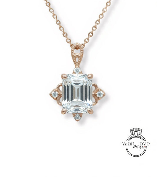 A necklace with a large, clear gemstone pendant, which appears to be a diamond. The pendant is set in a rose gold-colored metal and is part of a delicate chain.