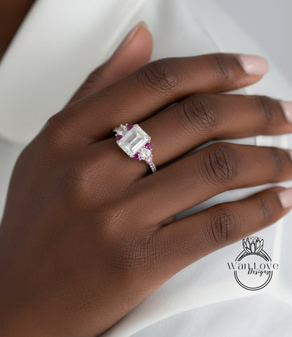 A close-up of a hand wearing a diamond engagement ring with a large central diamond surrounded by smaller diamonds and a pink gemstone.