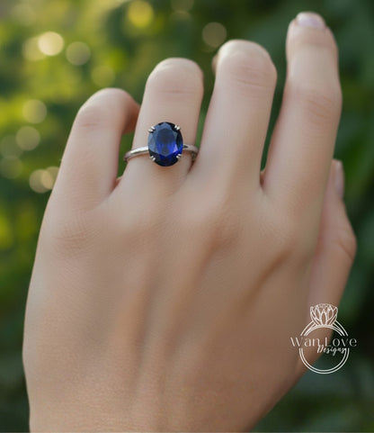 A close-up of a hand wearing a ring with a large blue gemstone, likely a sapphire, on the ring finger.