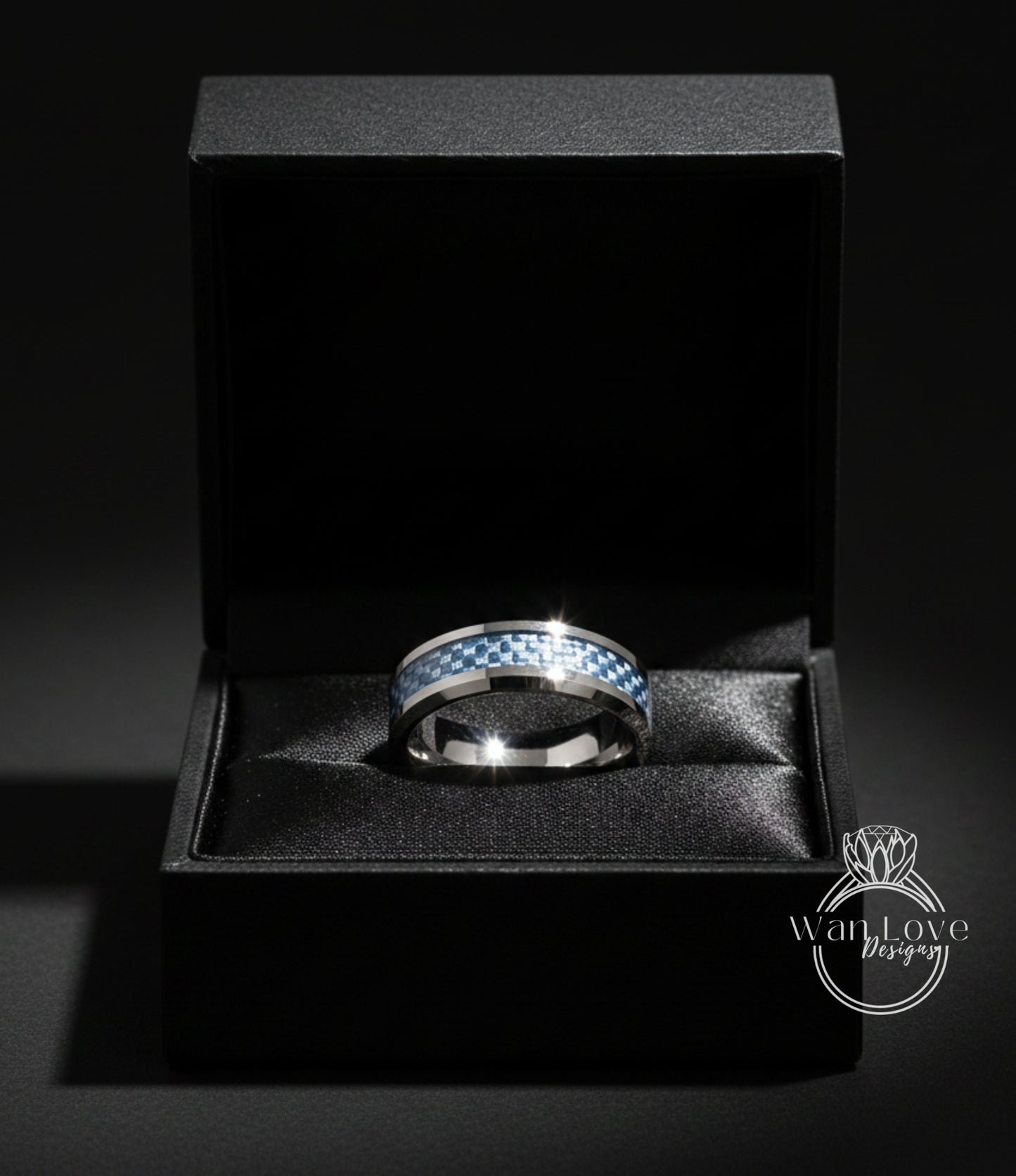A silver ring with a blue and white checkered pattern is displayed in a black jewelry box against a dark background.