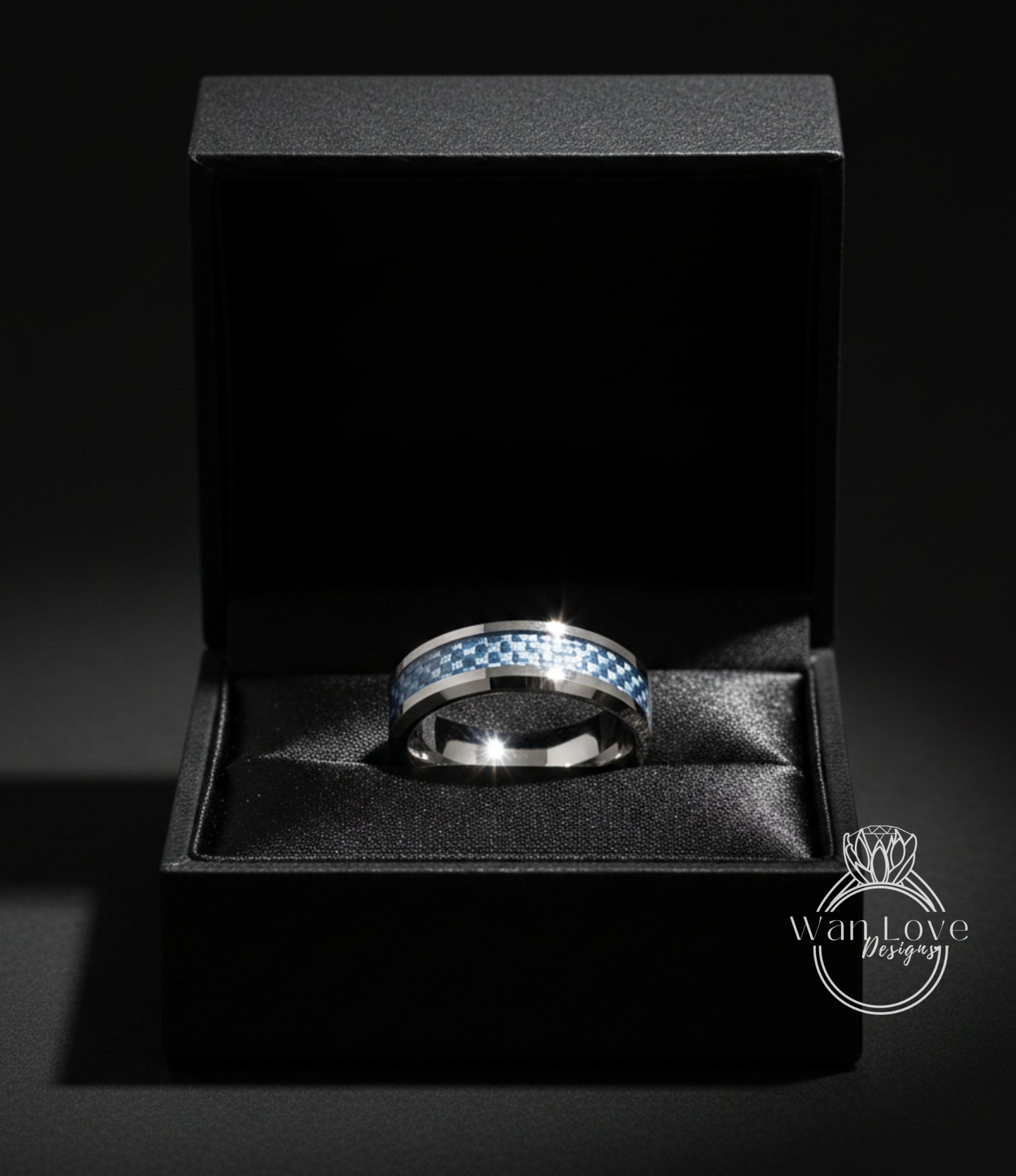 A silver ring with a blue and white checkered pattern is displayed in a black jewelry box against a dark background.