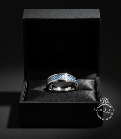 A silver ring with a blue and white checkered pattern is displayed in a black jewelry box against a dark background.