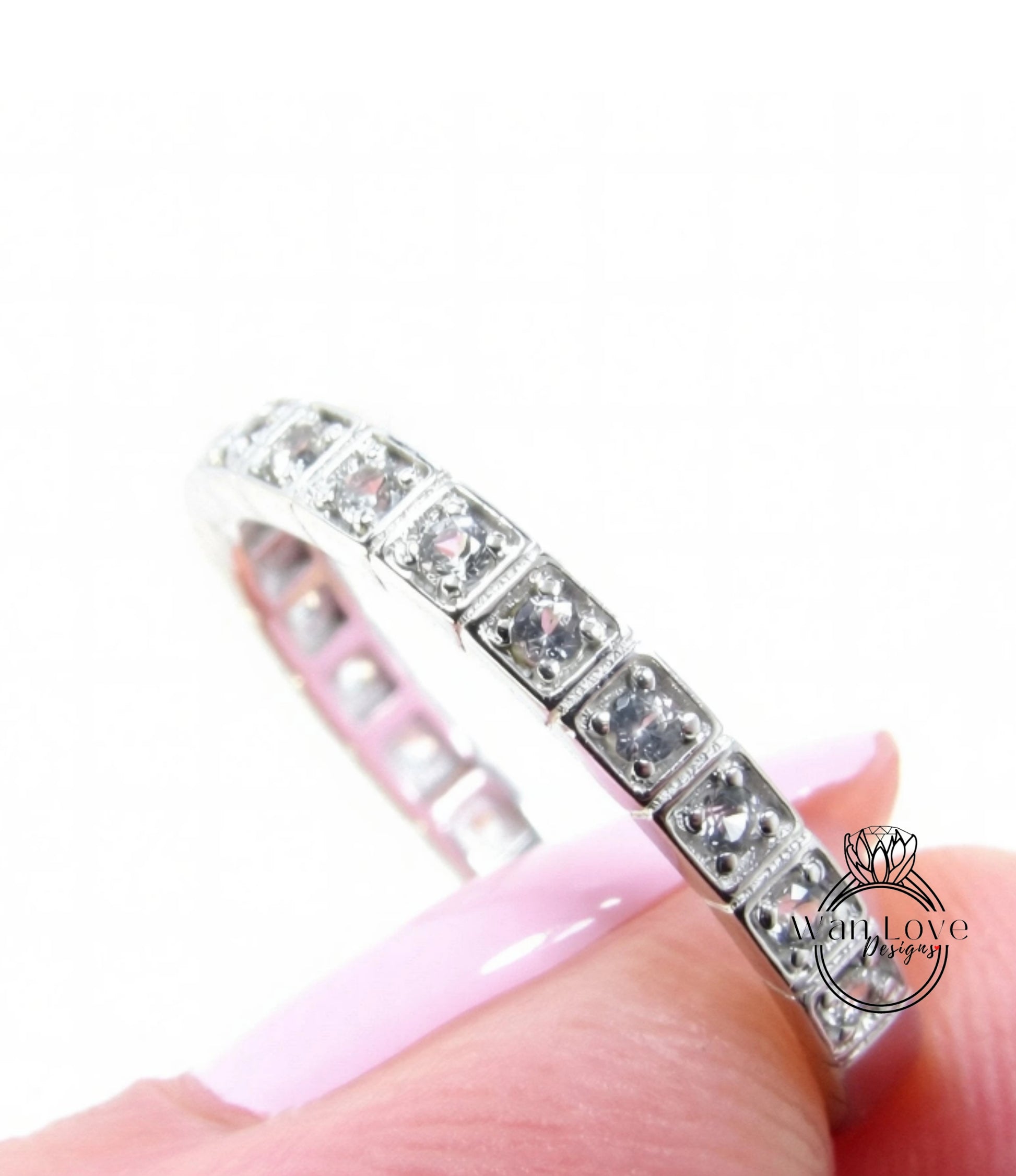 A close-up of a silver ring with a row of small diamonds set in it, held in someone's hand against a white background.