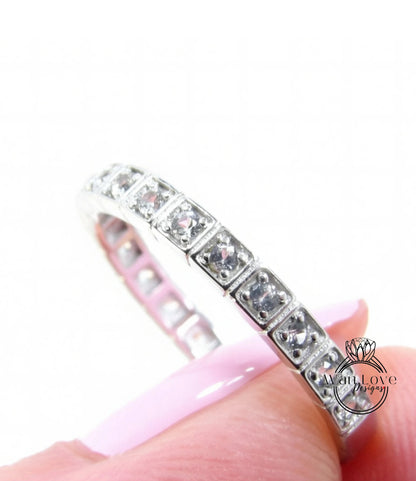 A close-up of a silver ring with a row of small diamonds set in it, held in someone's hand against a white background.