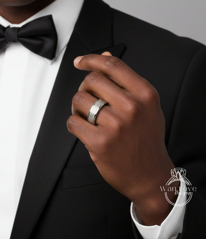 A close-up of a person's hand wearing a silver ring, with a black bow tie and a black suit jacket.