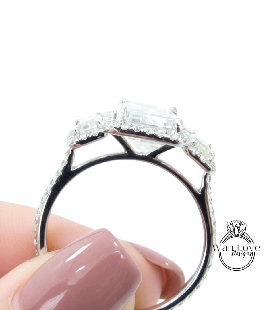 A close-up of a person's hand holding a diamond engagement ring with a large central diamond surrounded by smaller diamonds on the band.