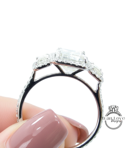 A close-up of a person's hand holding a diamond engagement ring with a large central diamond surrounded by smaller diamonds on the band.