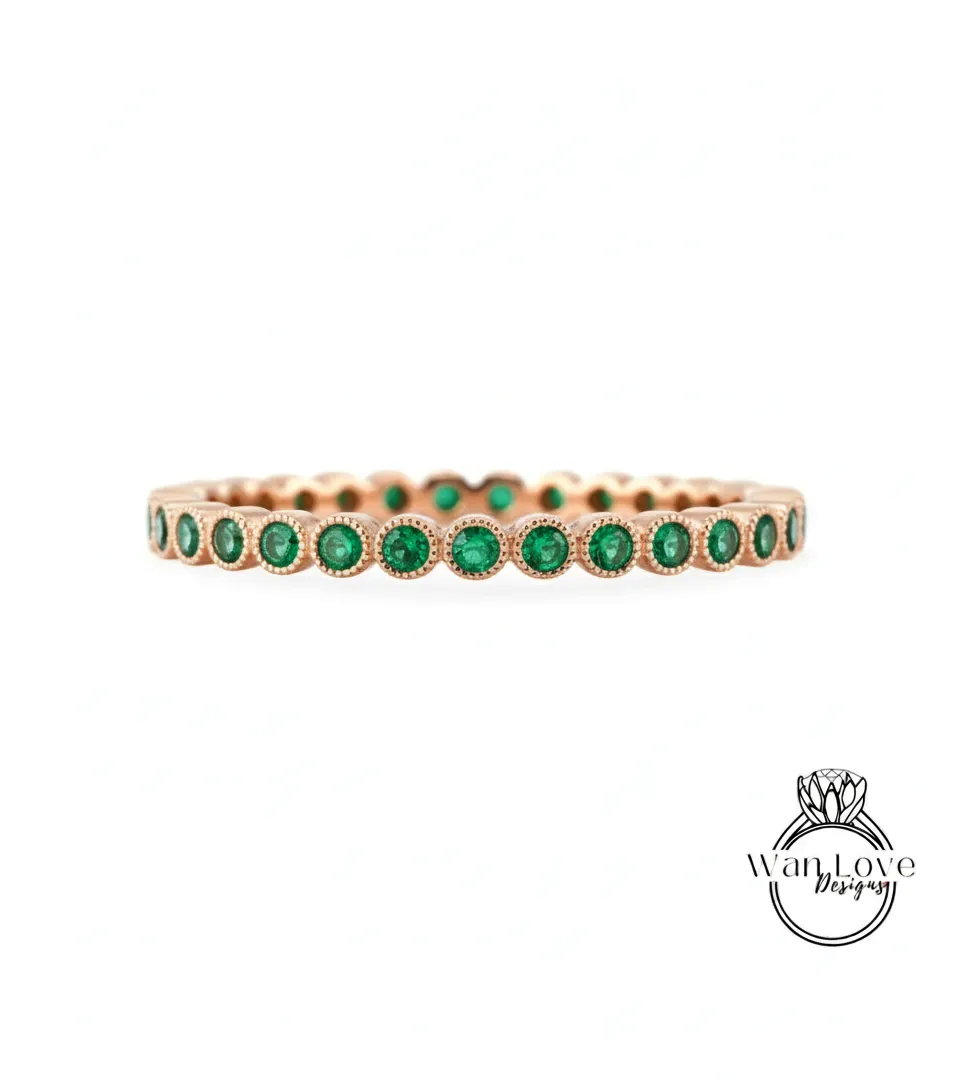 A gold-colored ring with a row of green gemstones, likely emeralds, set in the center.