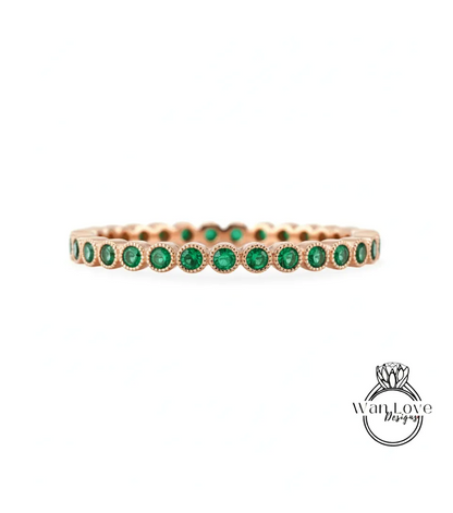 A gold-colored ring with a row of green gemstones, likely emeralds, set in the center.