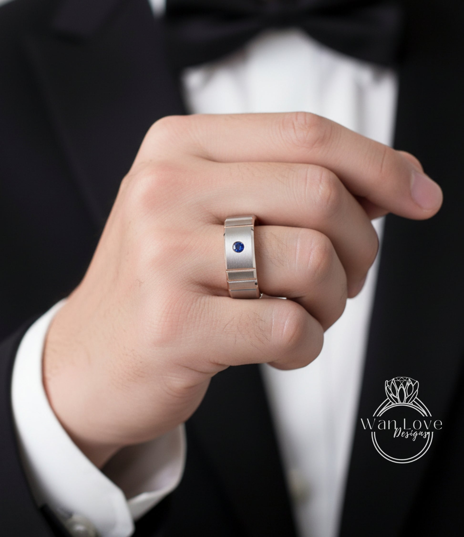 A close-up of a person's hand wearing a silver ring with a blue gemstone, wearing a black suit jacket.