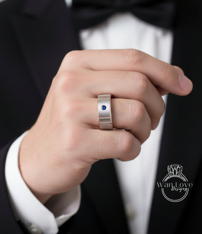 A close-up of a person's hand wearing a silver ring with a blue gemstone, wearing a black suit jacket.