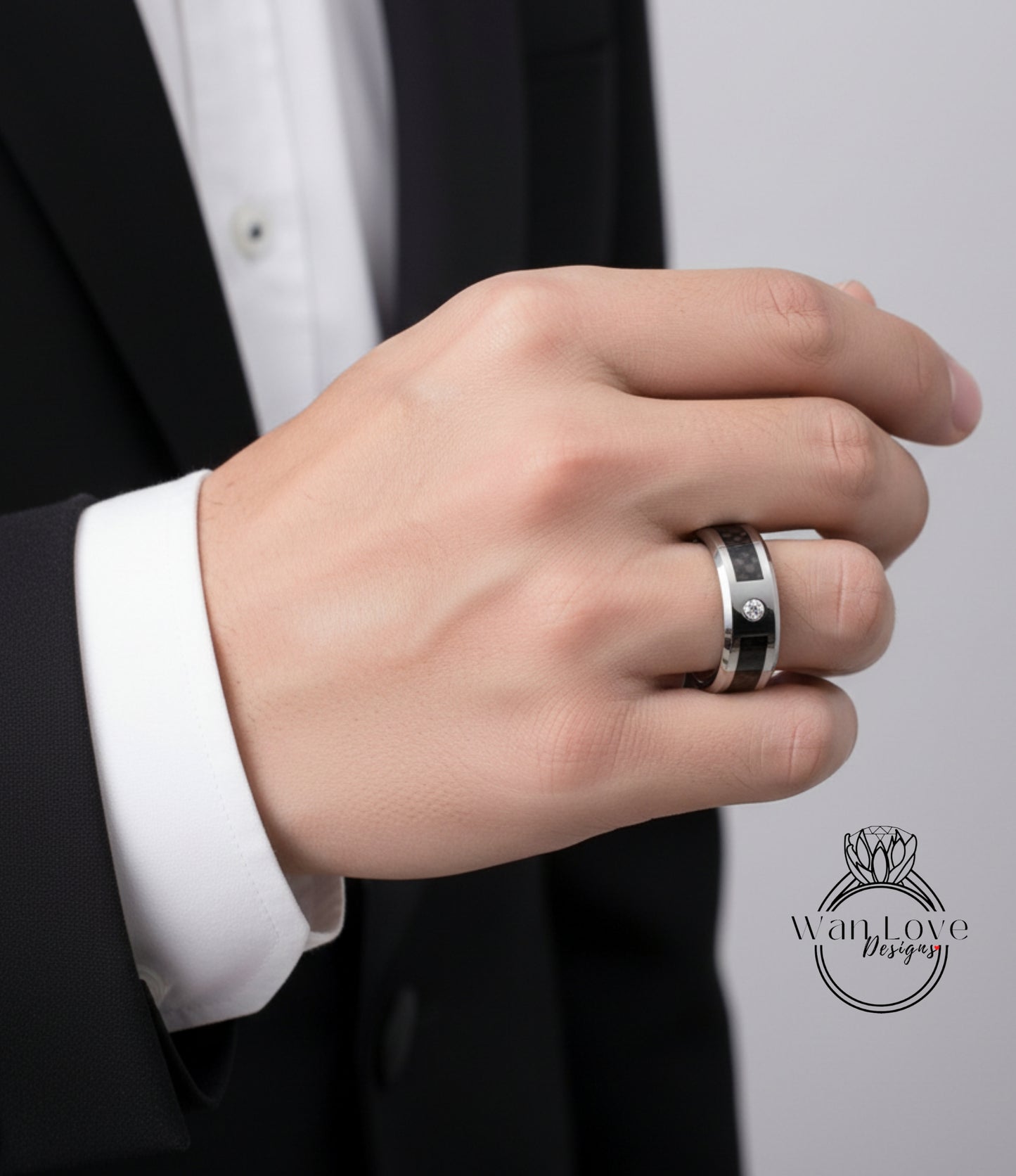 A close-up of a person's hand wearing a ring, with a black suit jacket visible in the background.