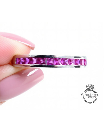 A hand holding a ring with a row of pink gemstones, likely rubies, set in a silver band.