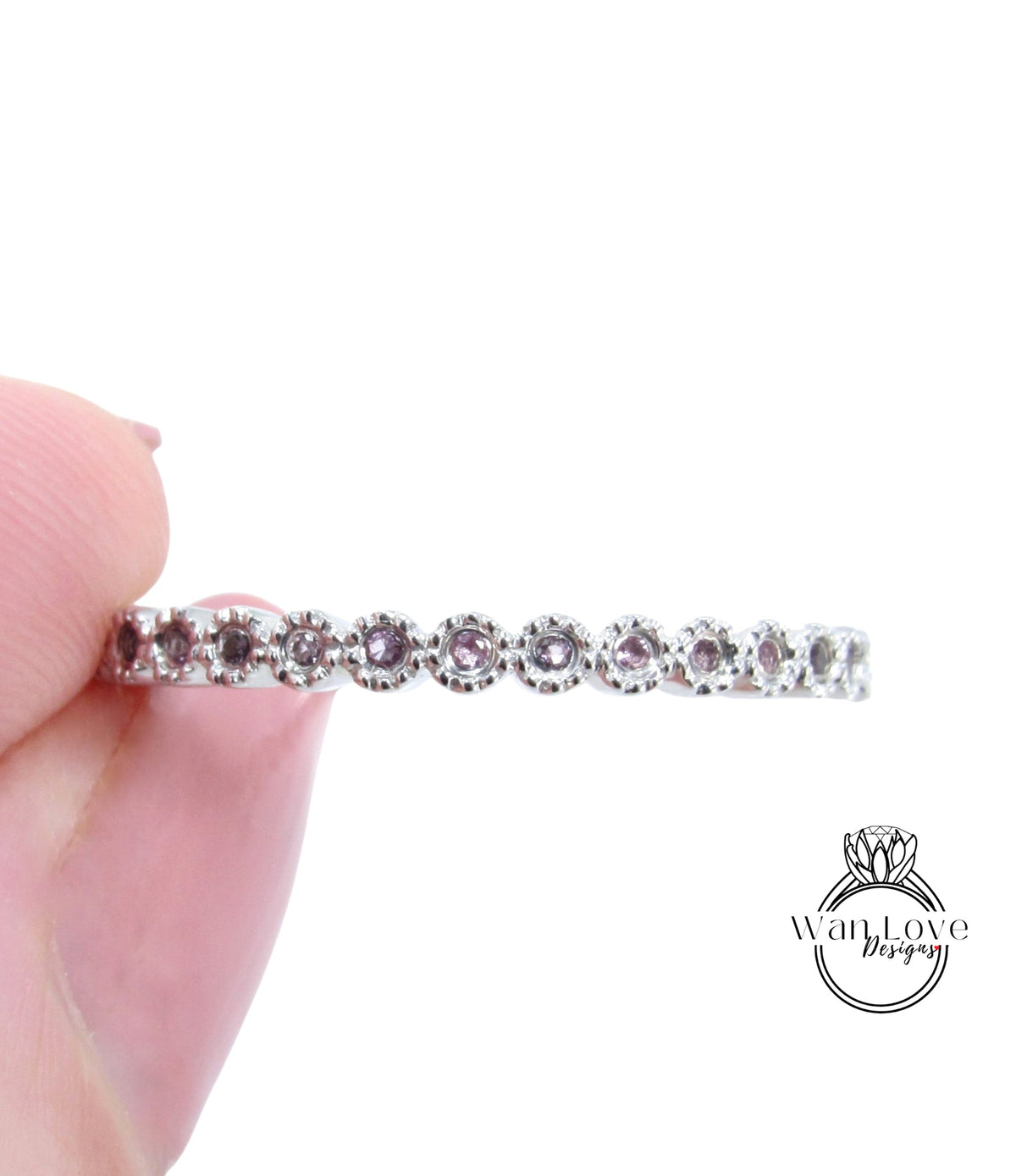 A hand holding a silver ring with a row of small, round, purple gemstones.