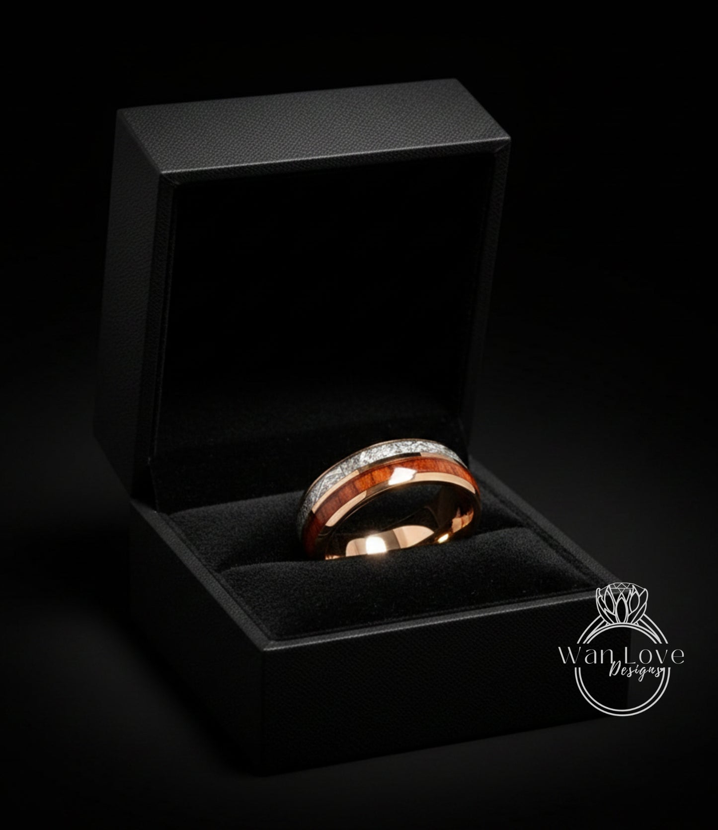 A gold ring with a red band and diamonds is displayed in a black jewelry box against a dark background.