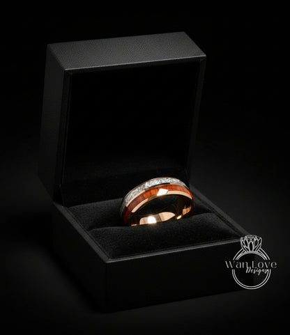 A gold ring with a red band and diamonds is displayed in a black jewelry box against a dark background.