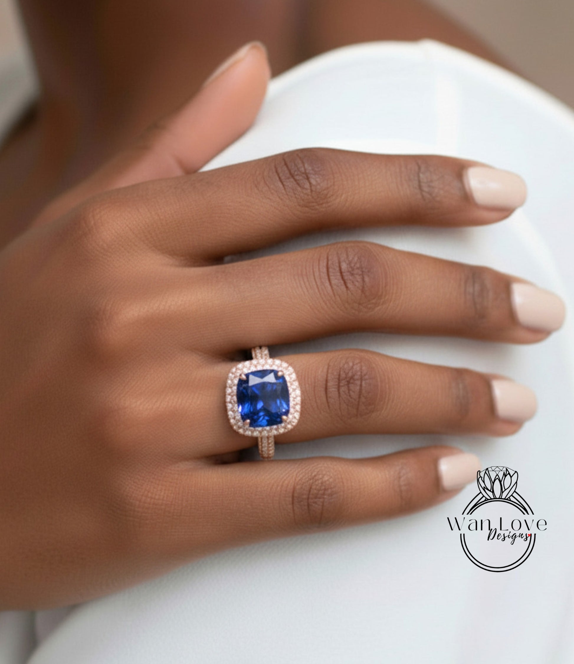 A close-up of a hand wearing a large, blue gemstone ring with a halo of smaller diamonds around it.