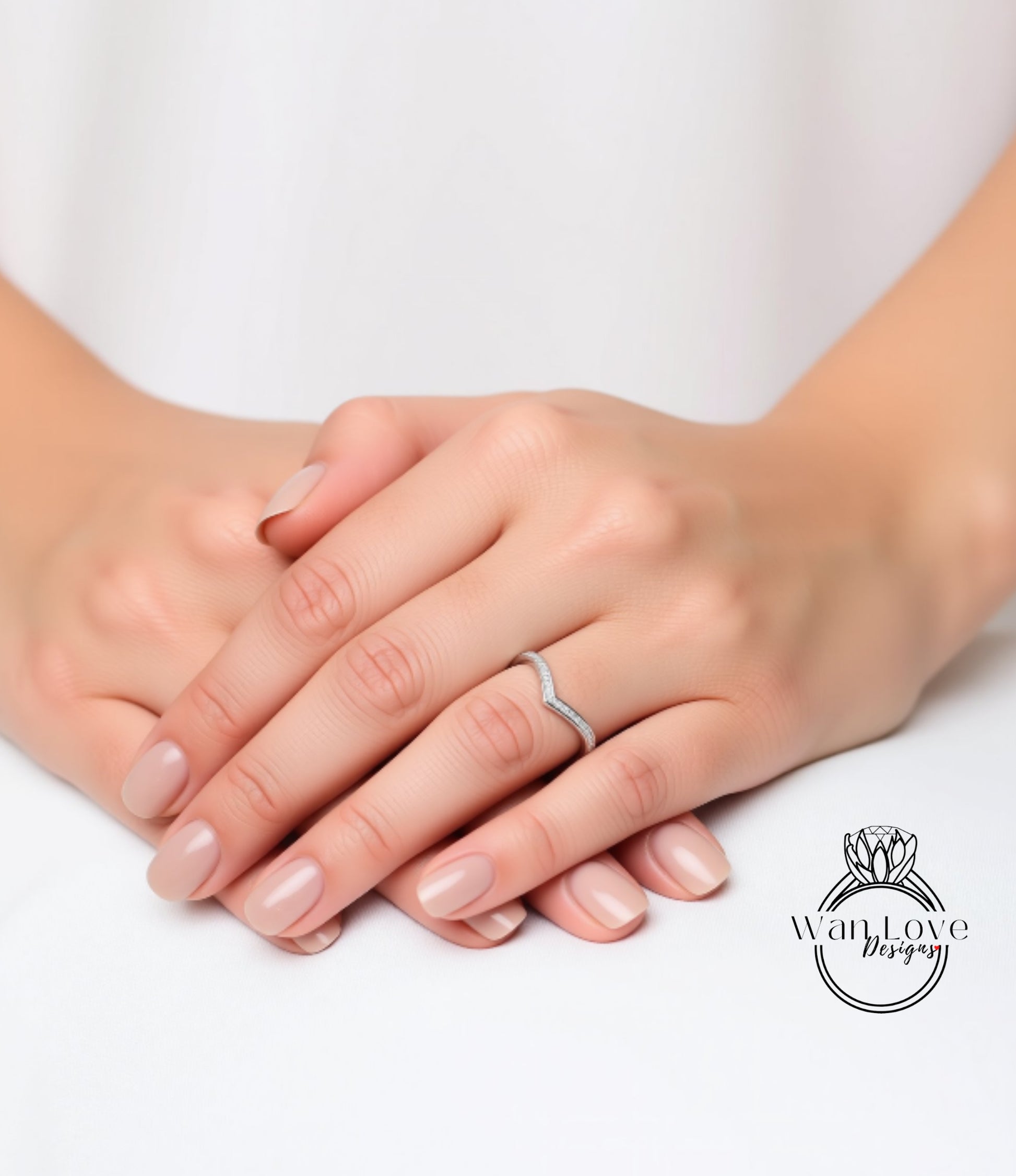 A close-up image of a person's hands with a ring on the ring finger, resting on a white surface.