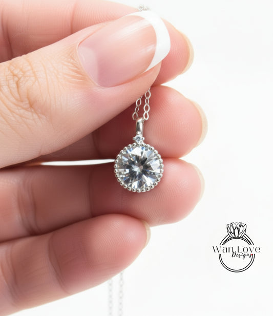 A hand holding a delicate necklace with a large, clear gemstone pendant.