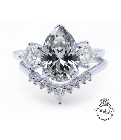 A stunning diamond engagement ring with a large pear-shaped diamond at the center, surrounded by smaller diamonds on either side. The ring is set in a silver band, and the background is a plain white color.