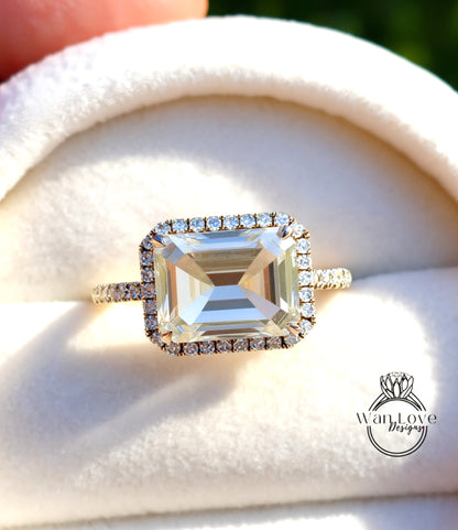 A large, clear gemstone ring with a halo of smaller diamonds around the center stone, placed on a white velvet background.