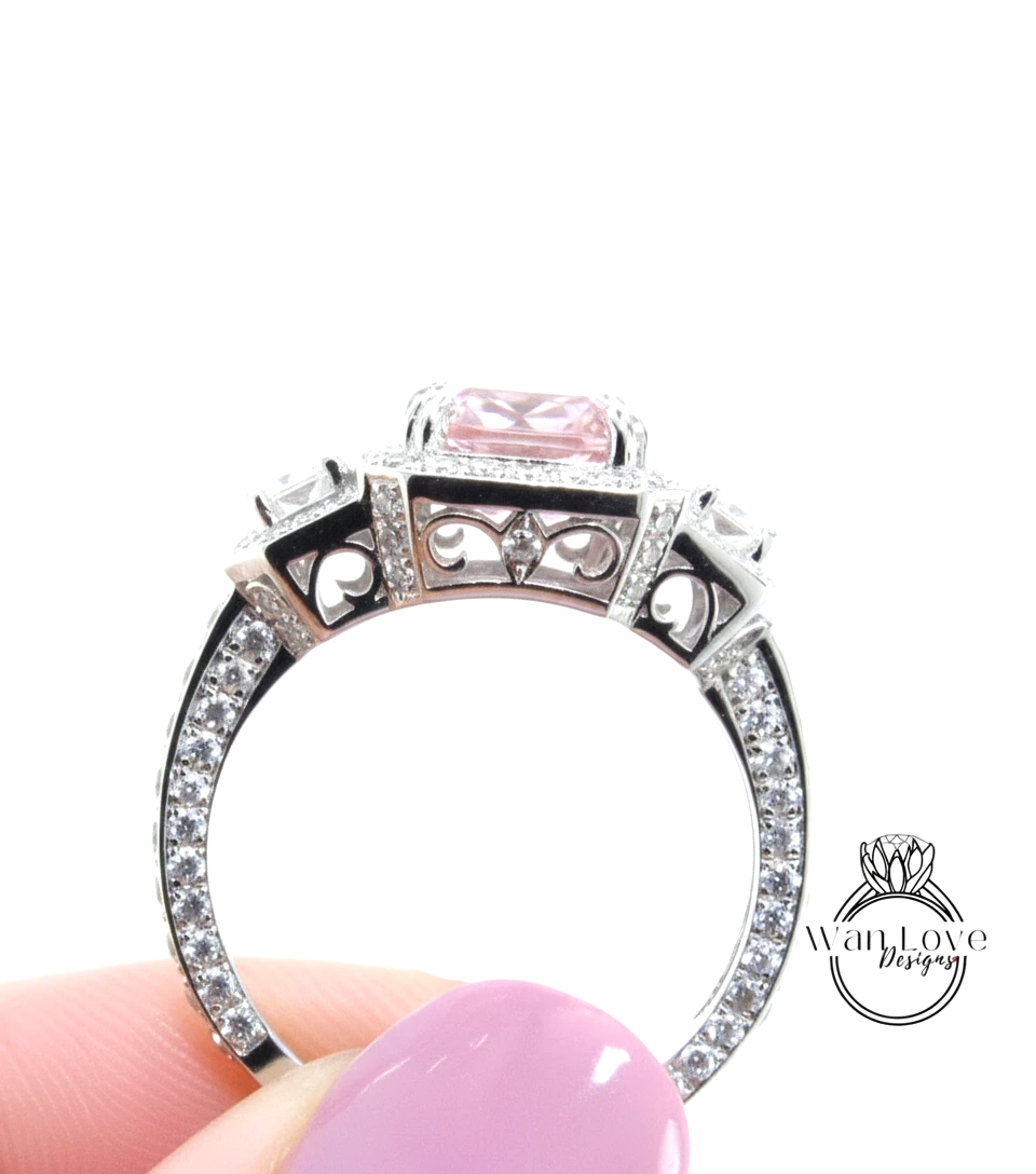 A close-up of a person's hand holding a silver ring with a pink gemstone, against a white background.