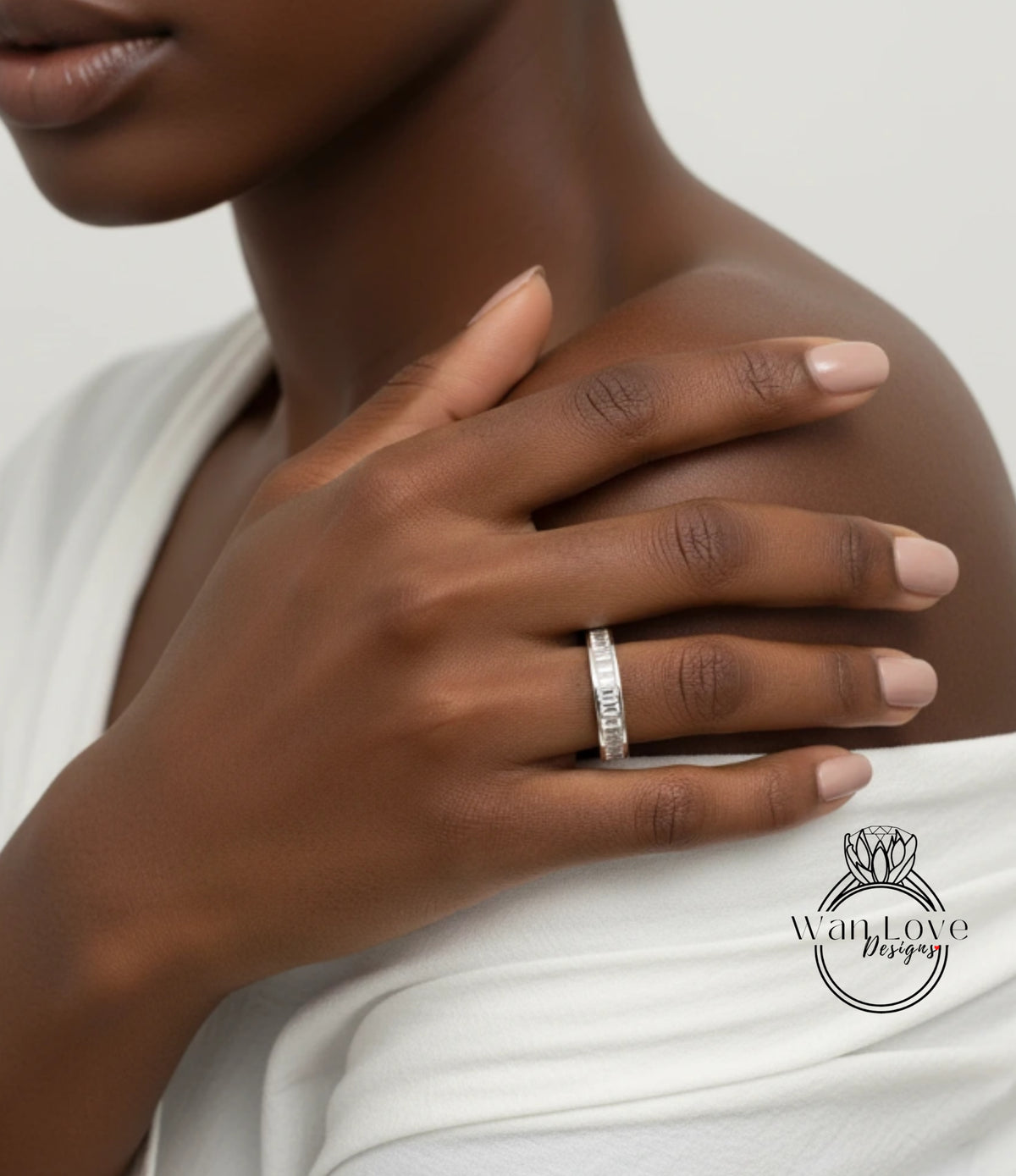 A close-up of a person's hand wearing a diamond ring, with their fingers gently resting on their shoulder.
