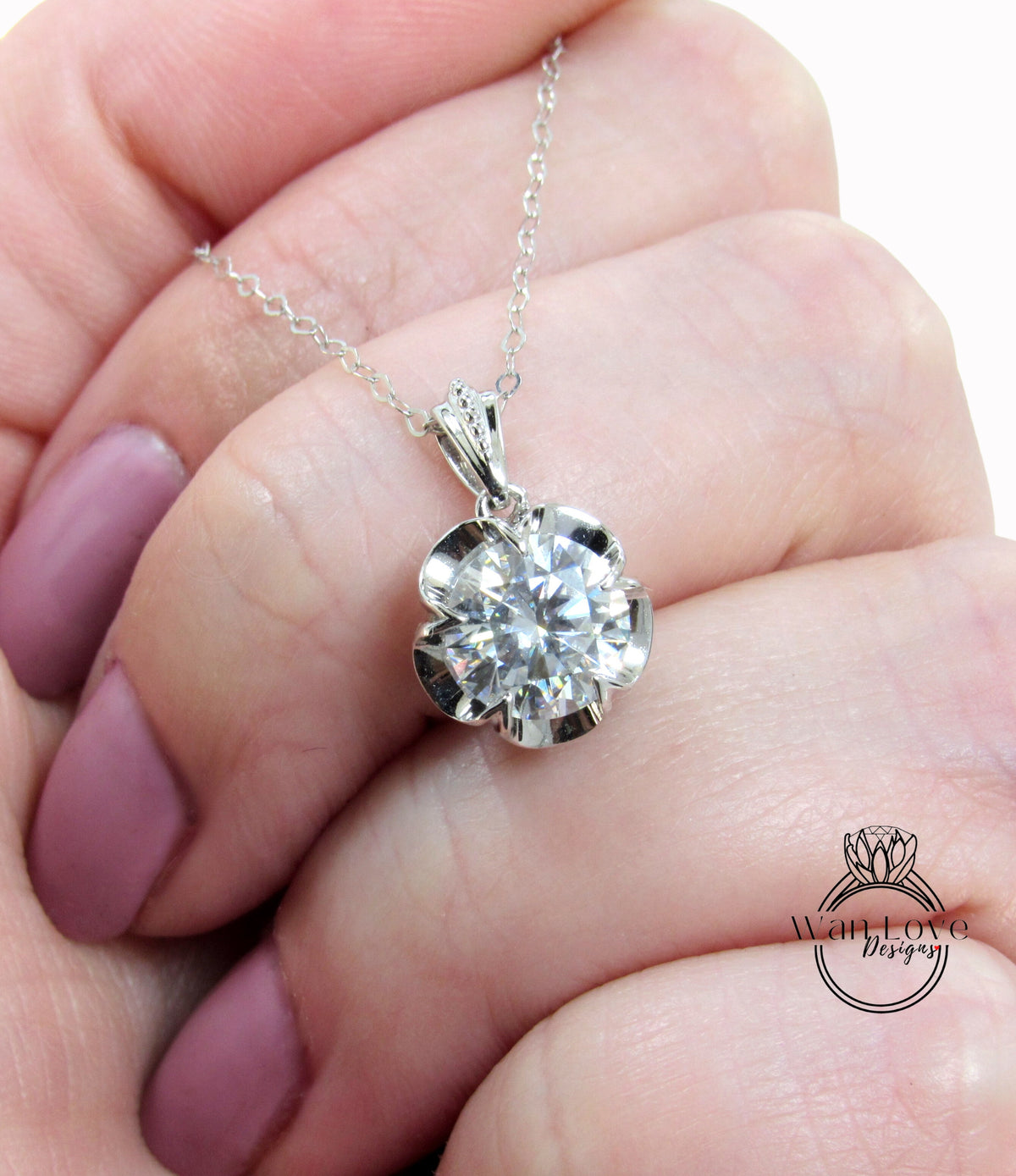 A close-up image of a person's hand holding a delicate silver necklace with a large, sparkling diamond pendant.