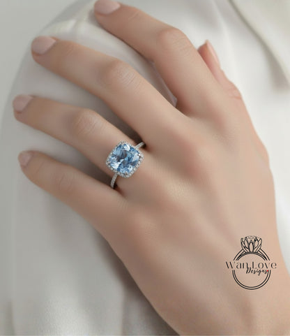 A close-up of a hand wearing a large, blue diamond ring with a halo.