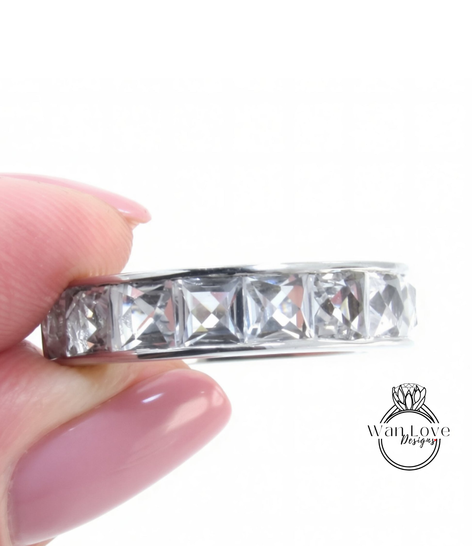 A close-up image of a person's hand holding a ring with a row of clear gemstones.