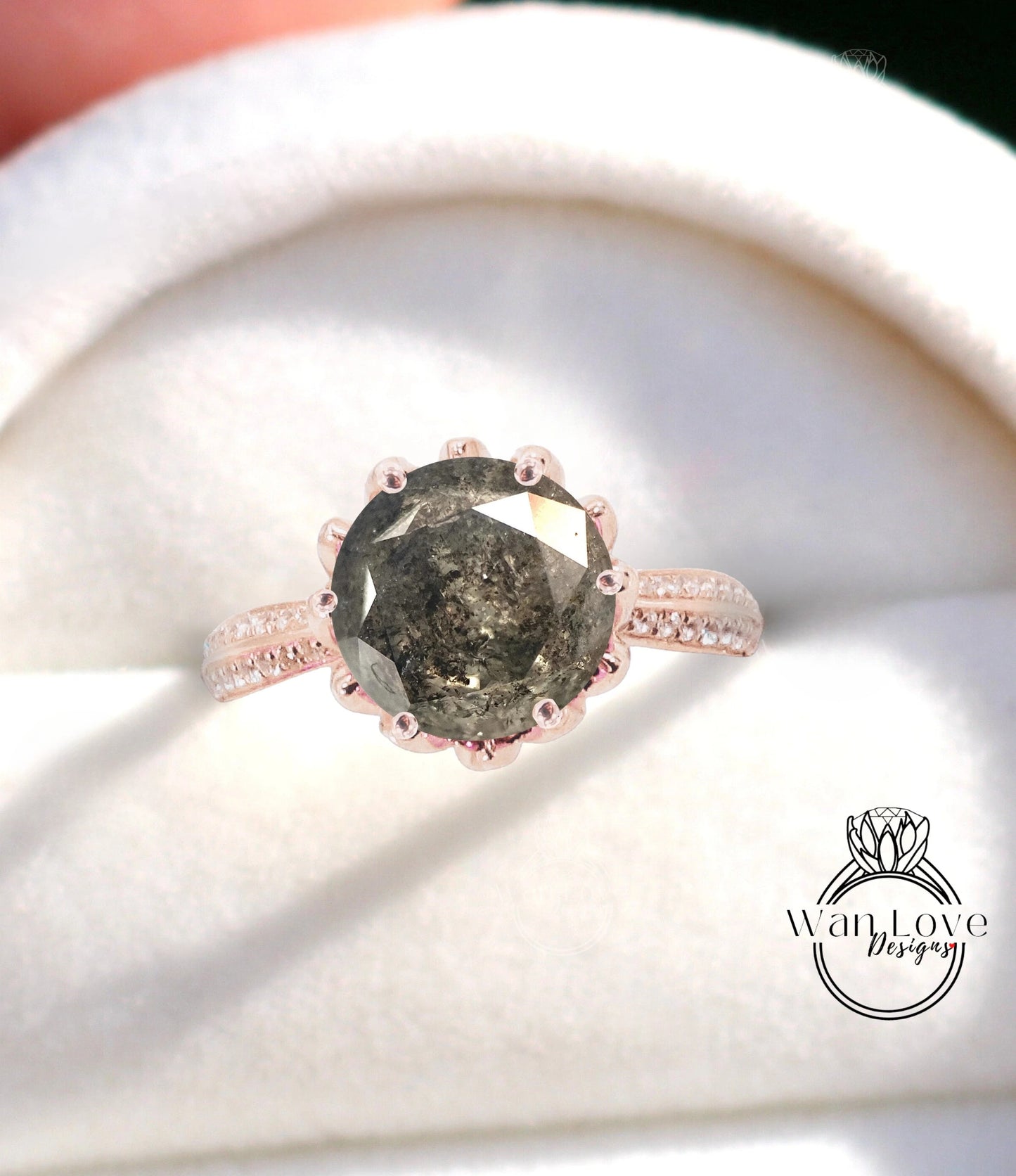 A close-up image of a large, dark grey diamond ring with a rose gold band and a white velvet background.