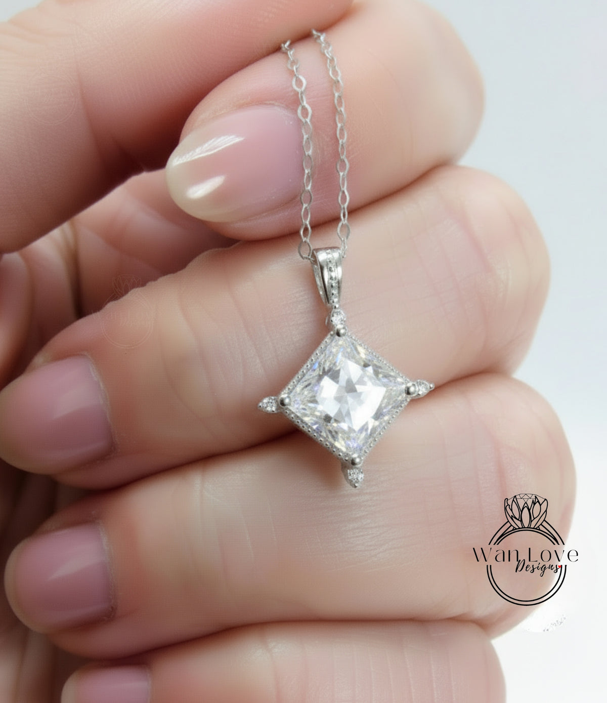 A close-up image of a person's hand holding a diamond pendant necklace with a large, clear gemstone.