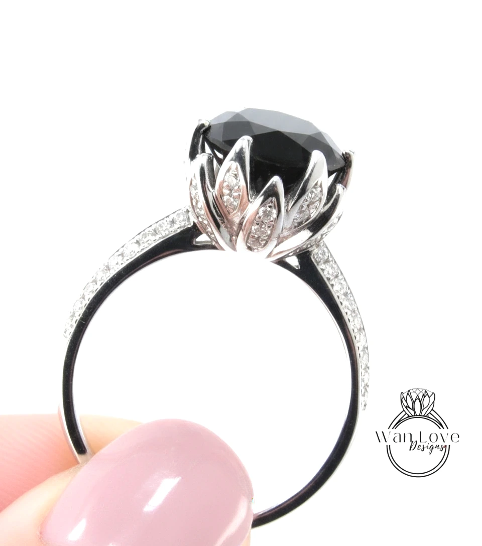 A close-up of a person's hand holding a silver ring with a large black gemstone, likely a diamond, and a decorative flower-like element.