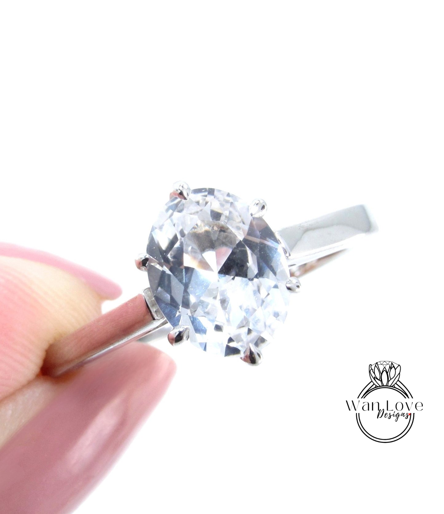 A close-up image of a person's hand holding a diamond engagement ring with a large oval-shaped diamond set in a silver band.