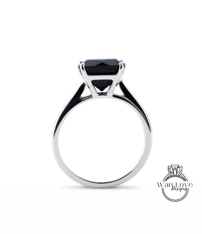 A silver ring with a large black gemstone, likely a diamond, set in the center.