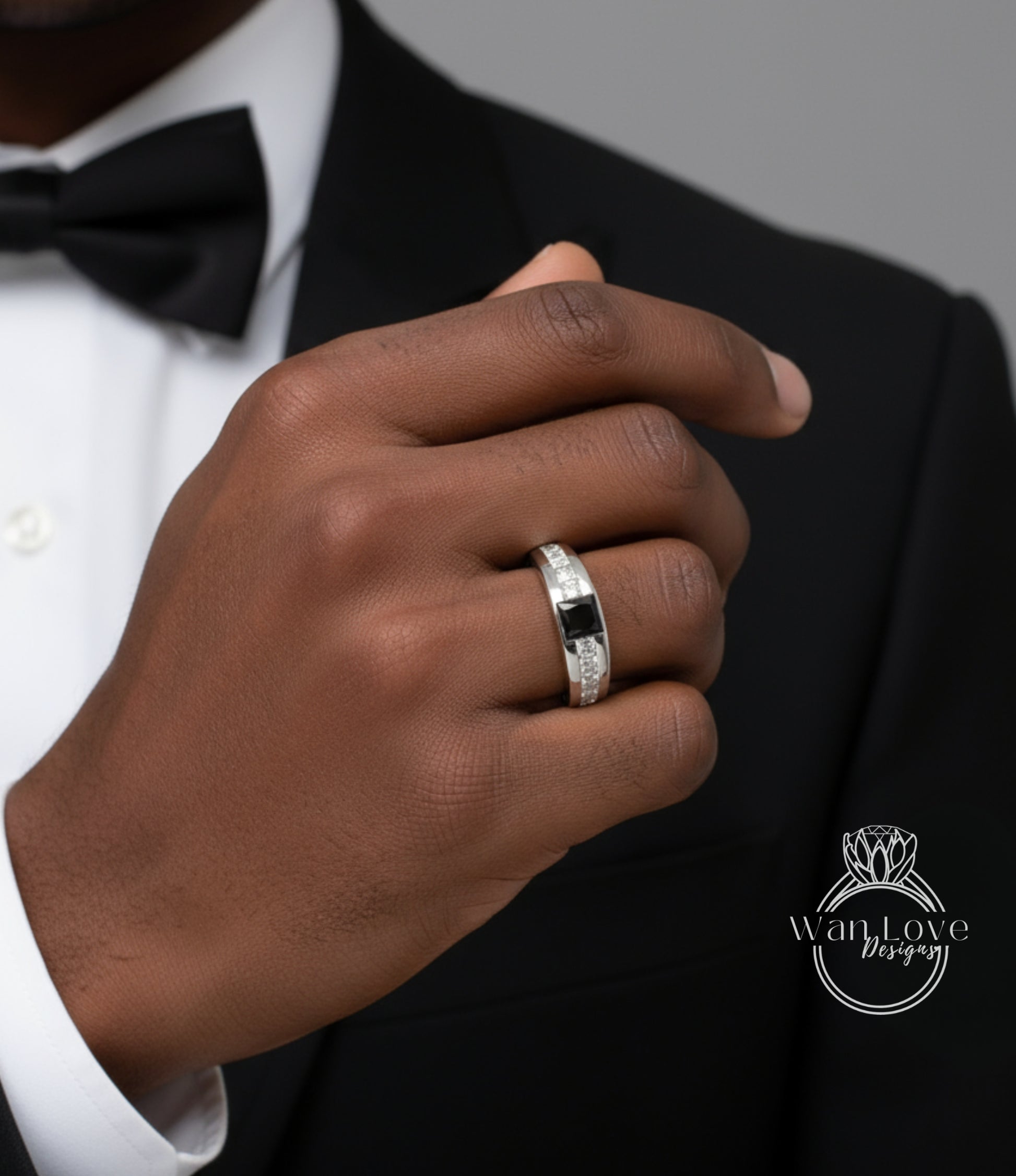 A close-up of a person's hand wearing a ring, with a black bow tie visible.