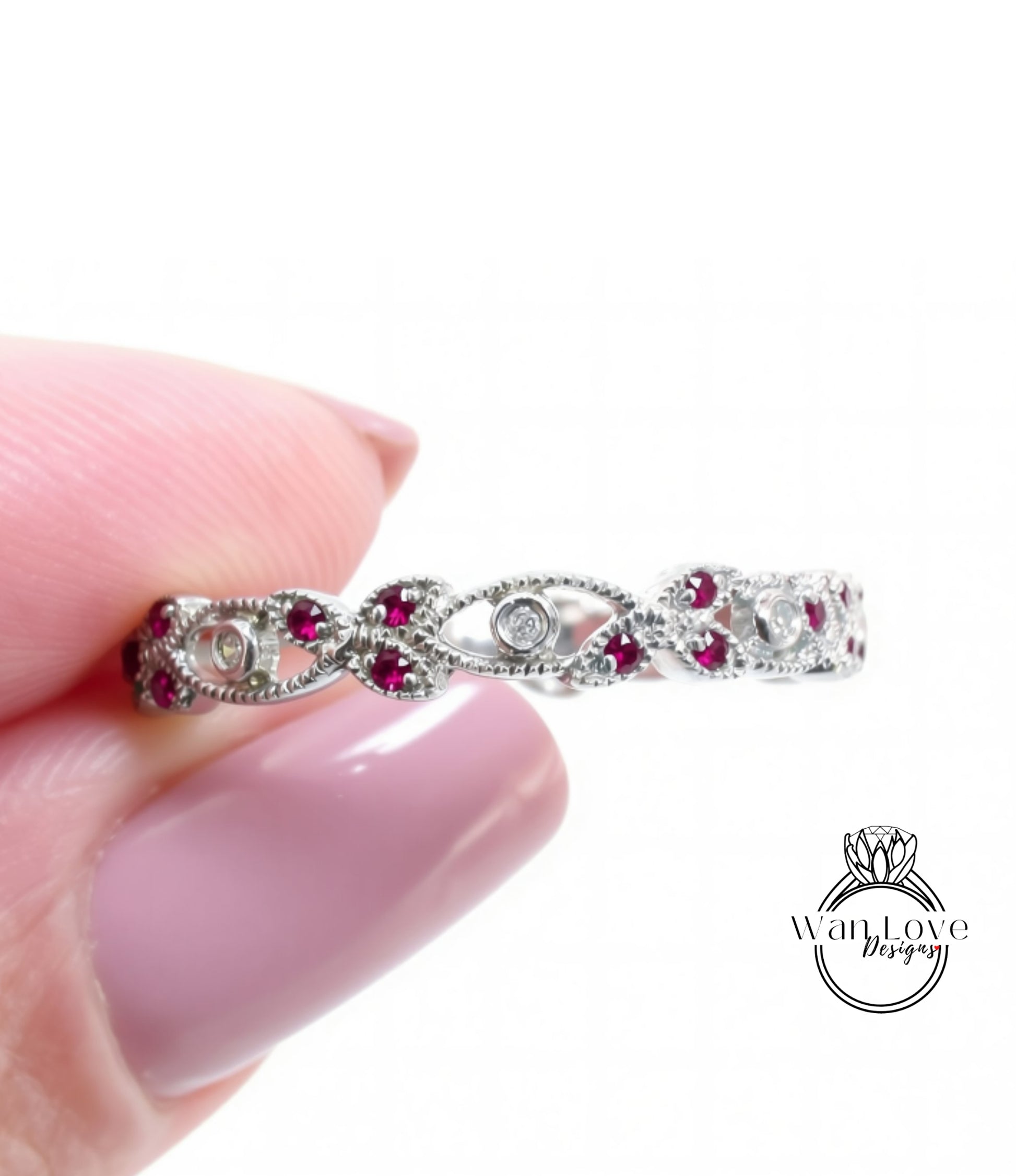 A close-up image of a person's hand holding a silver ring adorned with red gemstones.