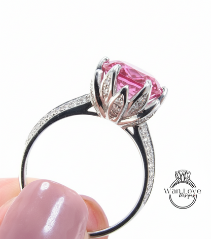 A close-up of a silver ring with a large pink gemstone, held in someone's hand.
