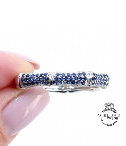 A close-up image of a person's hand holding a ring with a row of blue sapphires embedded in it.