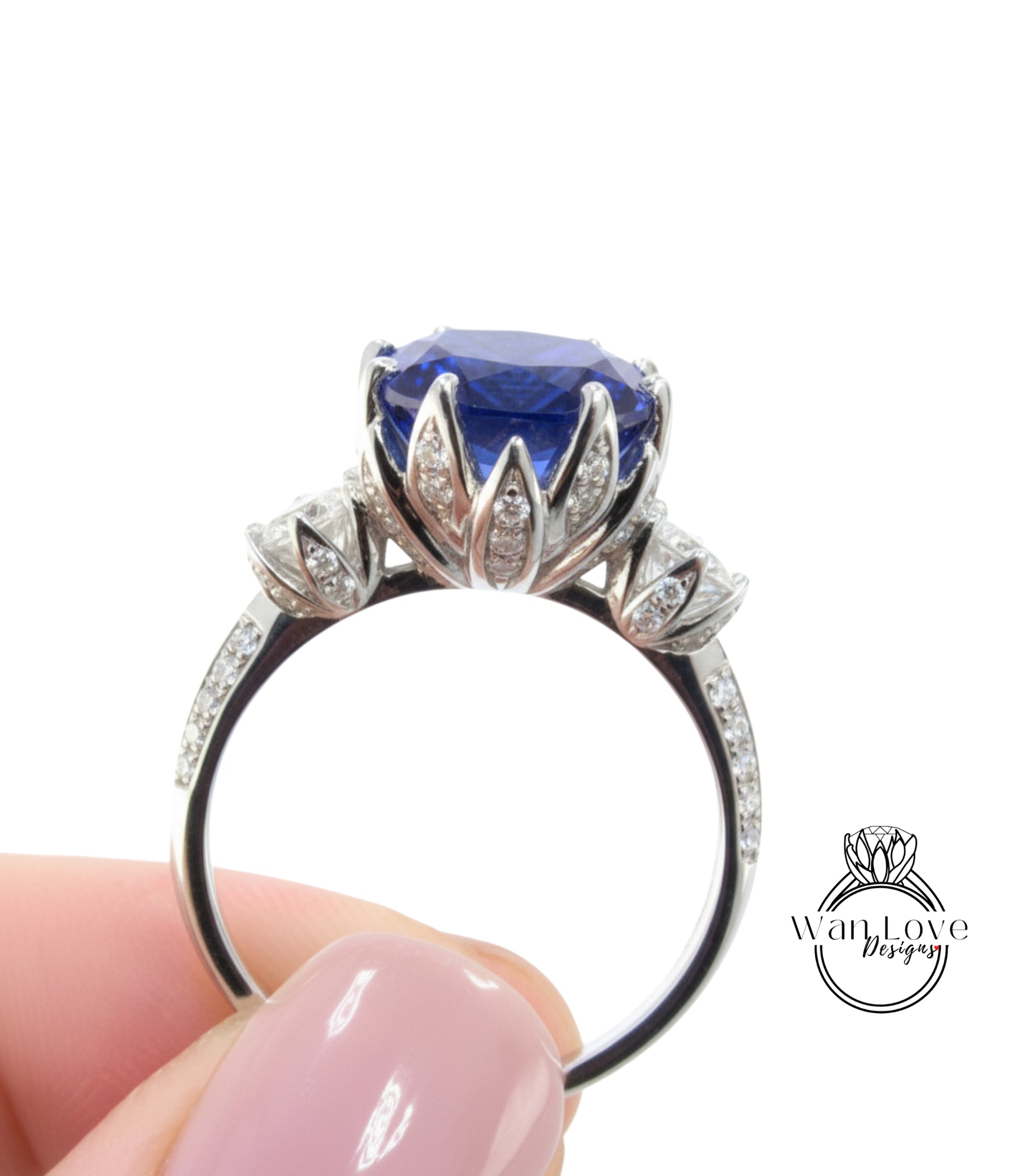 A close-up image of a person's hand holding a silver ring with a large blue gemstone, likely a sapphire, surrounded by smaller diamonds.