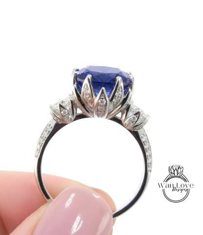 A close-up image of a person's hand holding a silver ring with a large blue gemstone, likely a sapphire, surrounded by smaller diamonds.